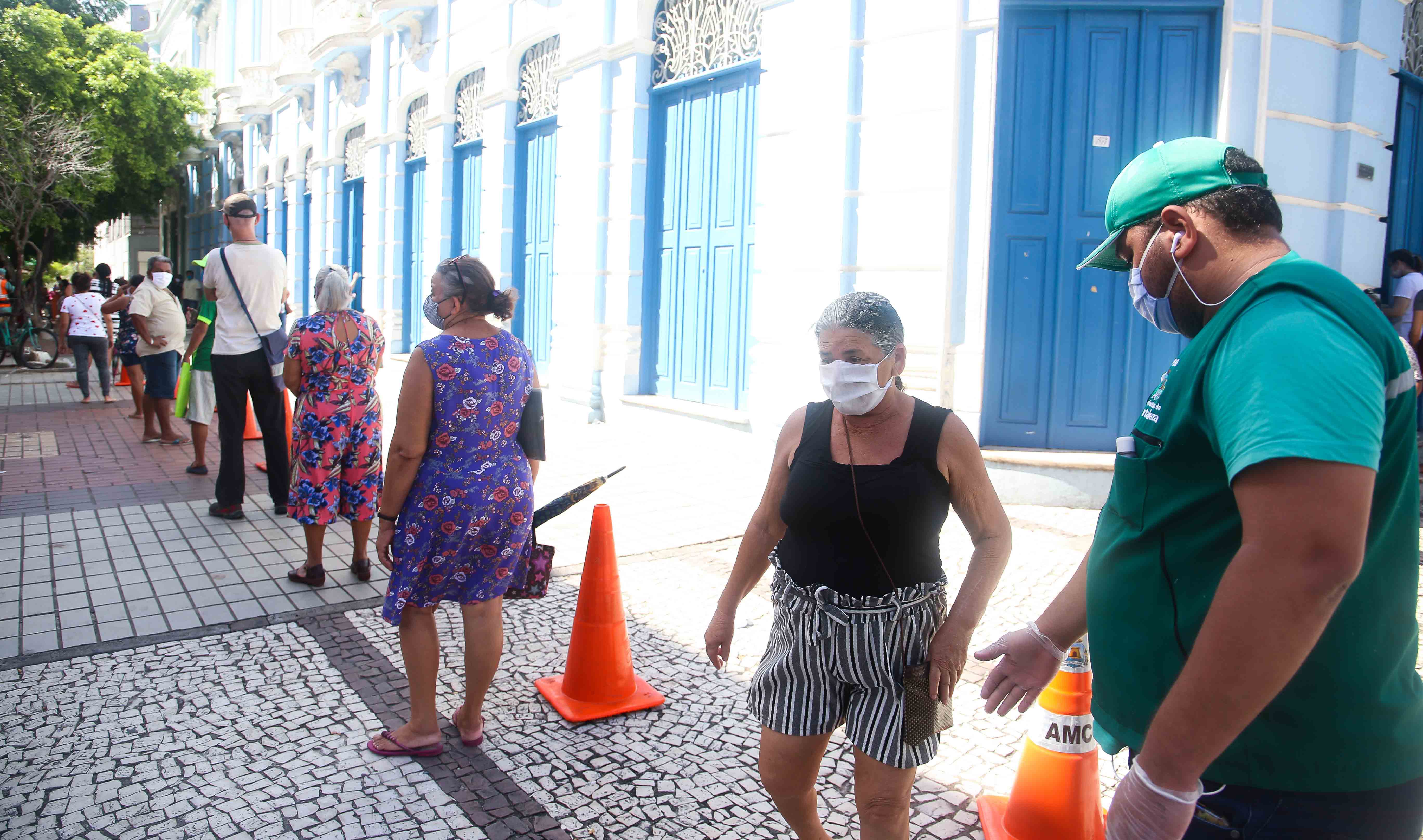 fiscal orientando pessoas a ficarem em suas posições em fila formada em praça